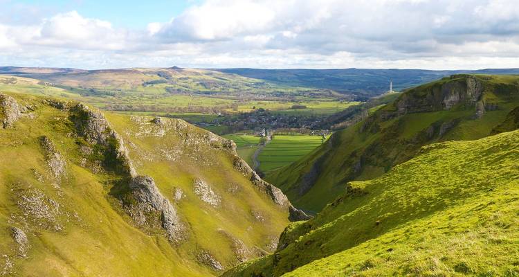 La vallée aux falaises calcaires vert dramatique s'ouvre sur les terres agricoles lointaines sous un ciel parsemé de nuages dans le Peak District.