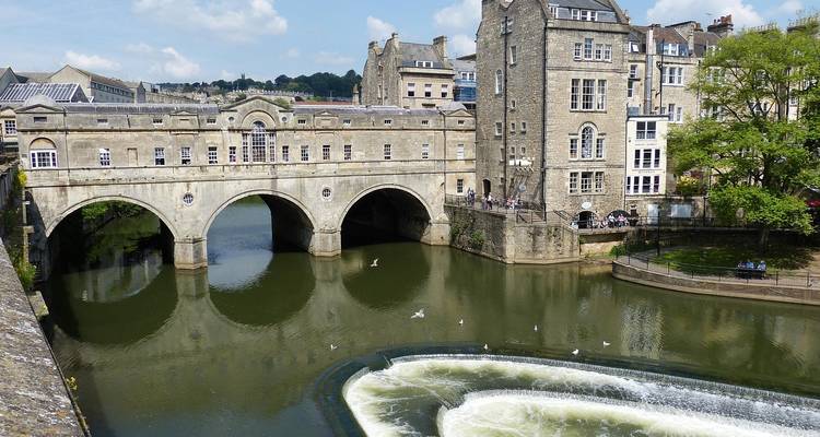 Historic Pulteney Bridge with Georgian buildings spans the River Avon beside cascading weir and gulls in Bath.