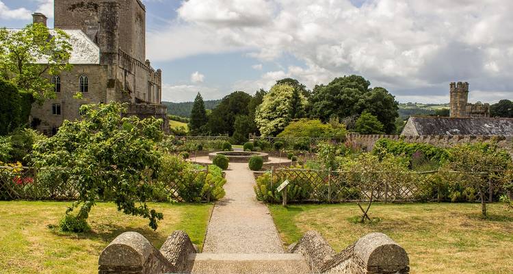 Formal garden with manicured hedges and a stone castle peeks through trees in rural Devon.
