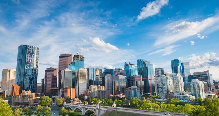 Bright skyline of Calgary with modern glass towers and Bow River bridge under a vivid blue sky.