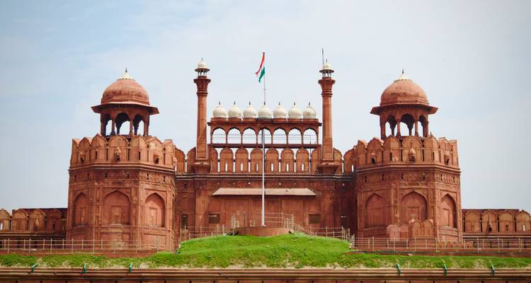 Vista frontal simétrica del Fuerte Rojo en Delhi con la bandera india ondeando bajo cielos despejados.