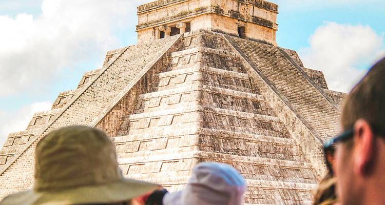 Temple pyramidal en pierre s'élevant sous un ciel lumineux avec des visiteurs rassemblés à sa base.