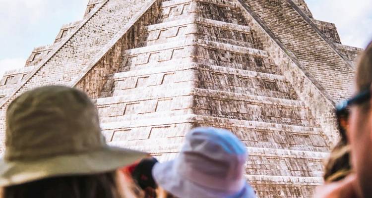 Close-up of the Pyramid of Kukulcán at Chichen Itza with tourists in hats looking up.