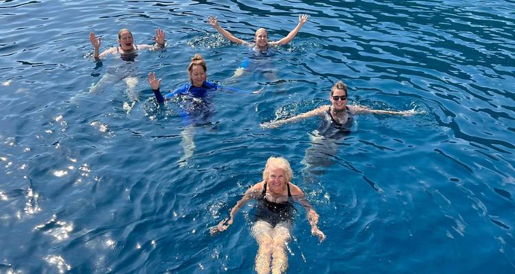 Cinq nageurs souriants flottant et agitant la main dans les eaux cristallines de la mer bleue.