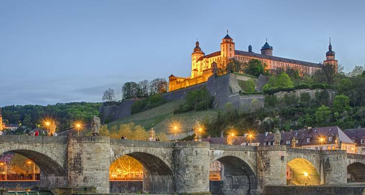 Marienberg Fortress illuminated at dusk above an old stone bridge in Würzburg, Germany.