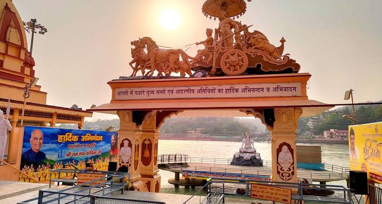 Arche décorée au bord de la rivière avec sculpture de char illuminée par le soleil surplombant le Gange et une statue de Shiva.