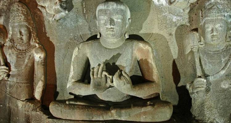 Des statues de pierre sculptées de divinités assises à l'intérieur d'un ancien temple creusé dans la roche, illuminées par une lumière douce.