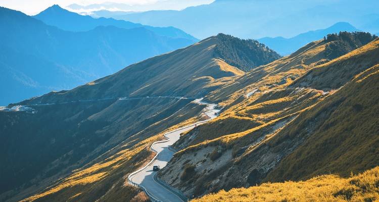 Gewundene Bergstraße schlängelt sich durch sonnenbeschienene alpine Grate unter dunstig blauen Gipfeln in Taiwan.