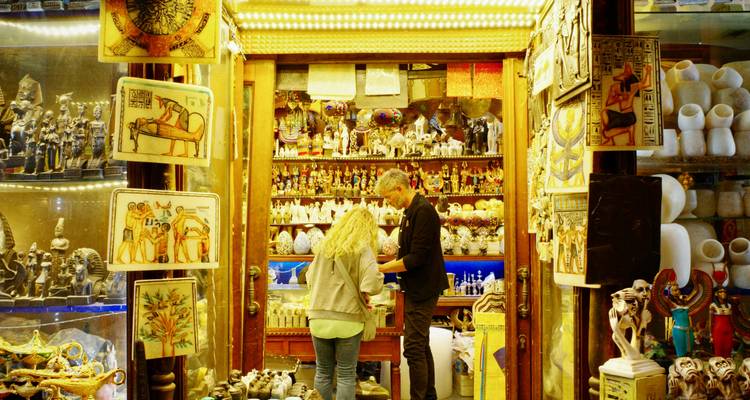 Warmly lit Egyptian souvenir shop filled with statues and papyrus art as a customer browses