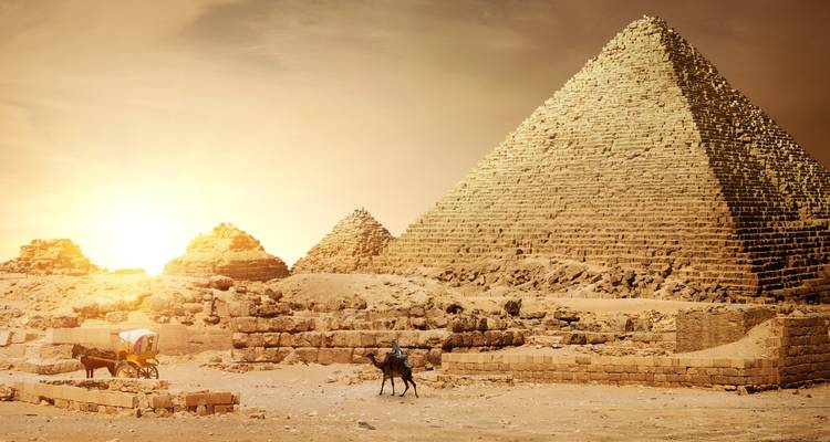 Golden sunset illuminates the Great Pyramid of Giza and surrounding ruins with a camel and carriage in the foreground