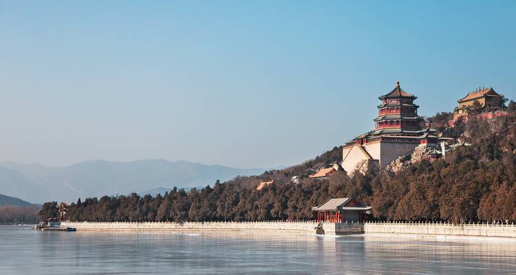 Complexe de pavillons chinois classiques dominant un lac tranquille avec des montagnes lointaines et brumeuses à l'horizon.