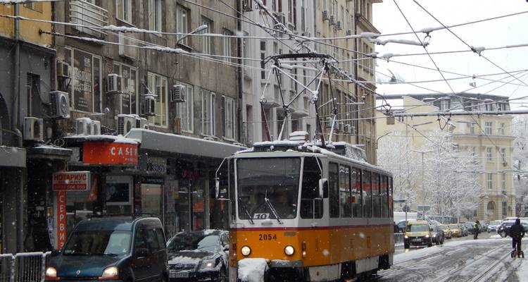 Le tramway orange qui se fraye un chemin dans une rue enneigée de Sofia bordée de voitures