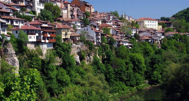 Les maisons en cascade de Veliko Tarnovo perchées sur une falaise surplombant une vallée fluviale verdoyante.