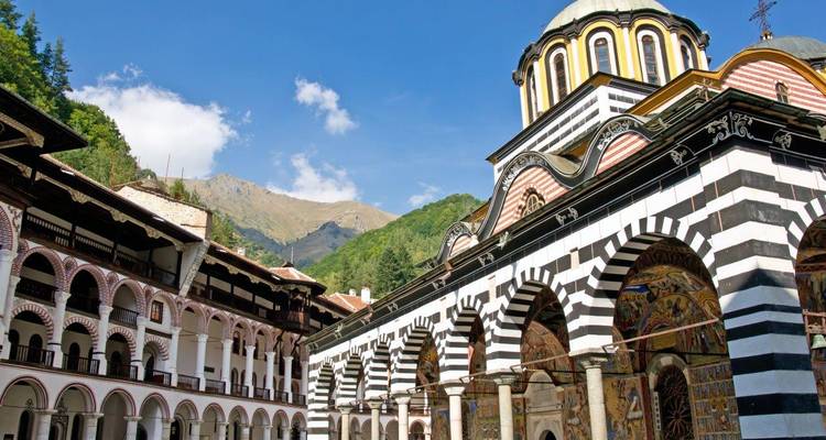 Les arches et dômes rayés colorés du monastère de Rila encadrés par des montagnes boisées.