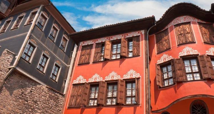 Des maisons de la Renaissance bulgare peintes de couleurs vives avec des volets en bois ornementés sous un ciel bleu.