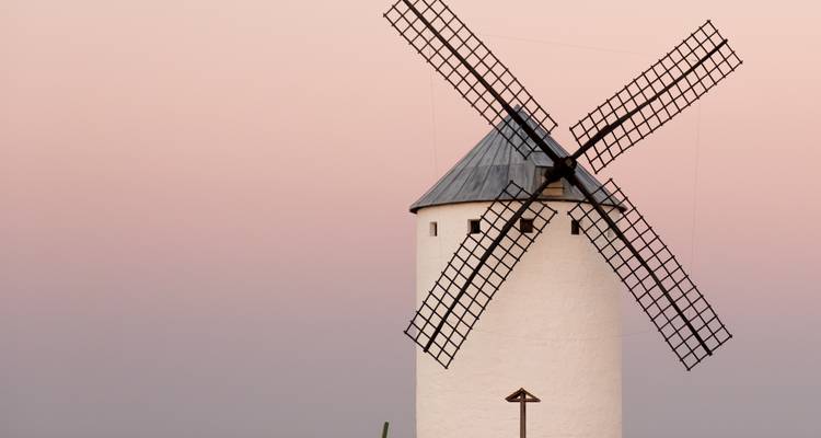 Klassische weiße Windmühle mit Gitterflügeln, die sich gegen einen sanften rosa Abendhimmel abzeichnet.