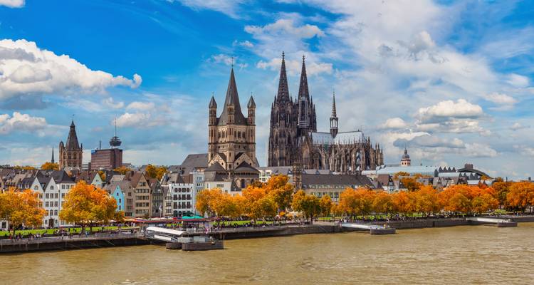 Vue panoramique du front de mer historique de Cologne avec les flèches de la cathédrale s'élevant au-dessus des arbres d'automne.