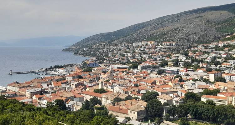 Panorama surélevé d'une ville adriatique aux toits rouges épousant le littoral avec les montagnes en arrière-plan