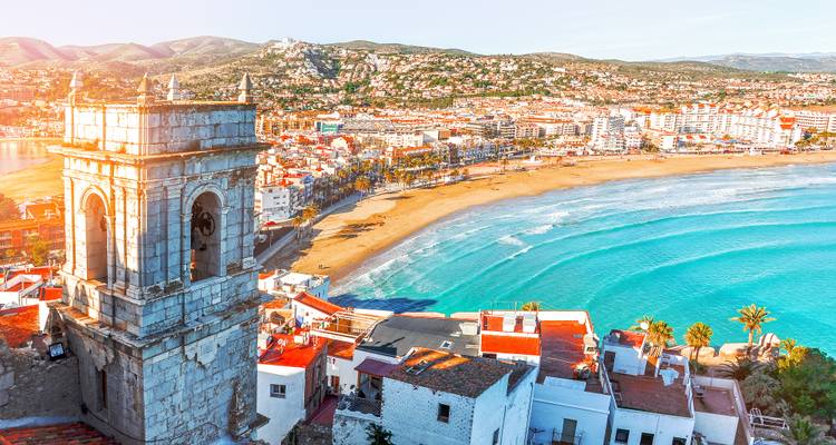 Coastal Spanish town with sandy beach, bright turquoise sea and a historic tower overlooking the bay.