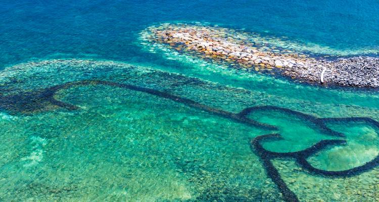 Aerial view of turquoise sea with heart-shaped traditional fishing traps and rocky breakwater