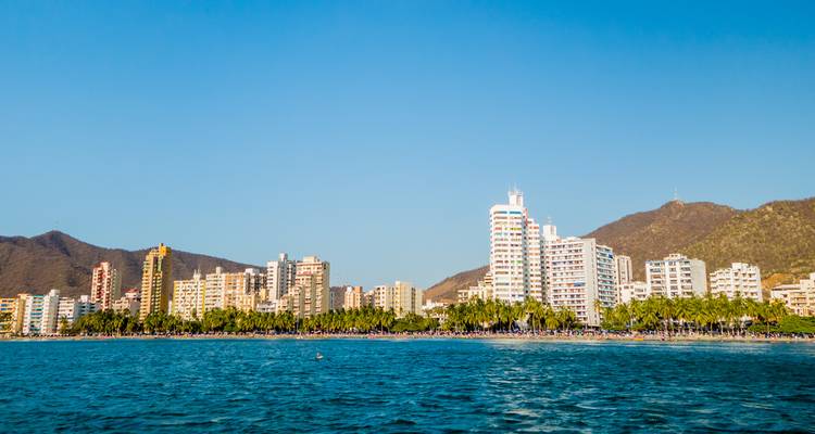 Large panorama du front de mer de Santa Marta encadré par une mer d'un bleu cristallin et des collines.