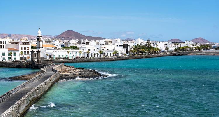 Vue sur les eaux turquoise en direction du phare d'Arrecife, de la jetée et des collines volcaniques lointaines.