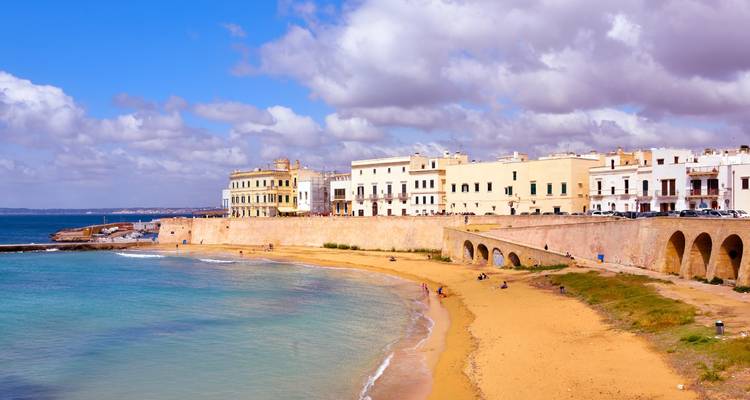 Sandy beach and fortified waterfront buildings of Gallipoli under a bright sky.