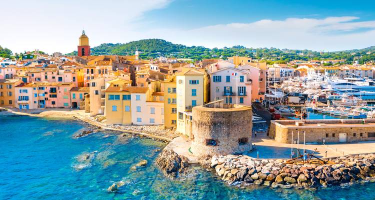 Vue panoramique du port de Saint-Tropez avec ses maisons aux couleurs pastel, la citadelle en pierre et les yachts sous un soleil éclatant.