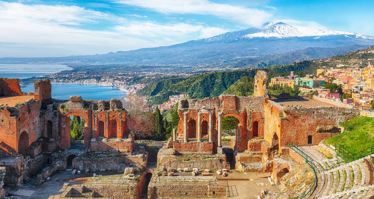 Ruinas de un antiguo teatro greco-romano en Taormina con vistas a la costa siciliana y el Mont Etna con sus cimas nevadas.