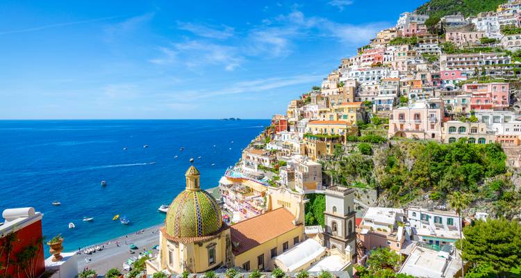 Colorful cliffside village of Positano cascading toward the deep blue sea with the iconic tiled dome in foreground.