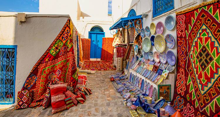 Ruelle aux couleurs saturées à Sidi Bou Said présentant des tapis à motifs et des assiettes en céramique aux teintes éclatantes en vente.