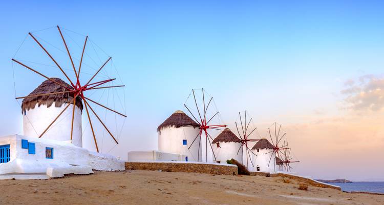 Rangée de moulins blancs emblématiques aux toits de chaume sur une crête sableuse à Mykonos à la lumière douce du soir.