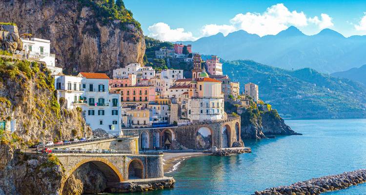 Village pittoresque d'Amalfi aux falaises colorées avec route côtière en arche et montagnes s'élevant à l'arrière-plan.