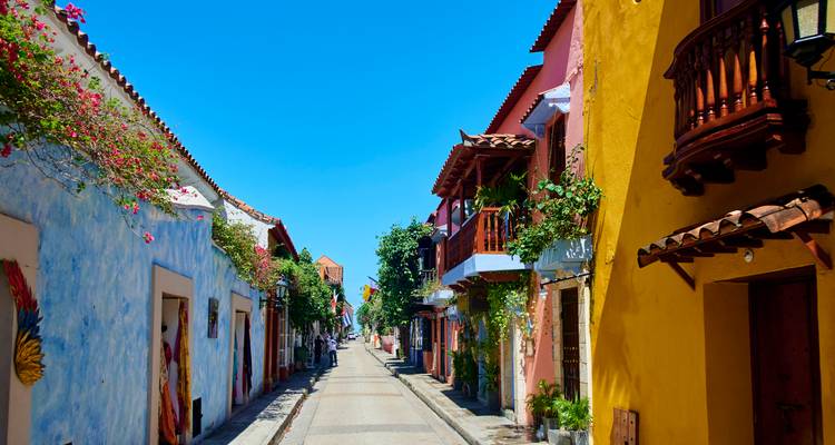 Ruelle coloniale étroite avec des maisons aux couleurs vives et des balcons fleuris sous un ciel dégagé.