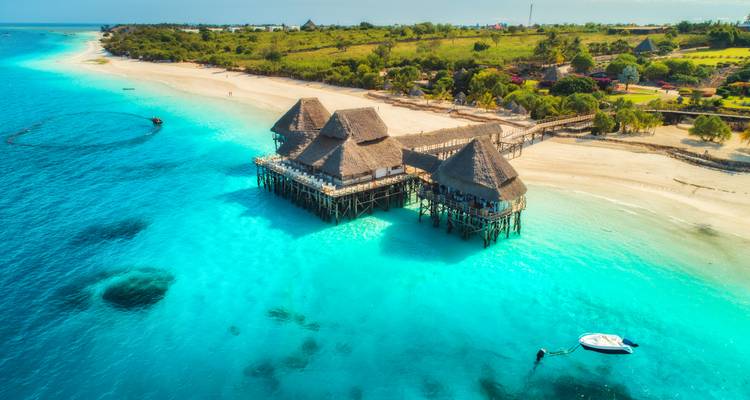 Bungalows sobre el agua en pilotes sobre una laguna turquesa cristalina y playa de arena blanca en la costa de Zanzíbar.