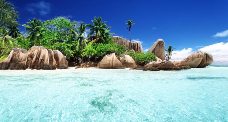 Icónicos bloques de granito y exuberantes palmeras elevándose desde el agua clara y poco profunda de la isla de La Digue.