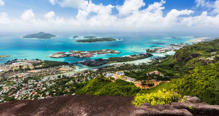 Vista aérea panorámica de las bahías turquesas de la isla de Mahé, pequeños islotes y montañas bajo nubes dispersas.