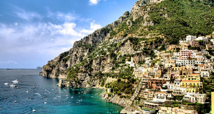 Pueblito dramático de Positano descendiendo por el acantilado hasta la costa turquesa de Amalfi con barquitos esparcidos por la bahía.