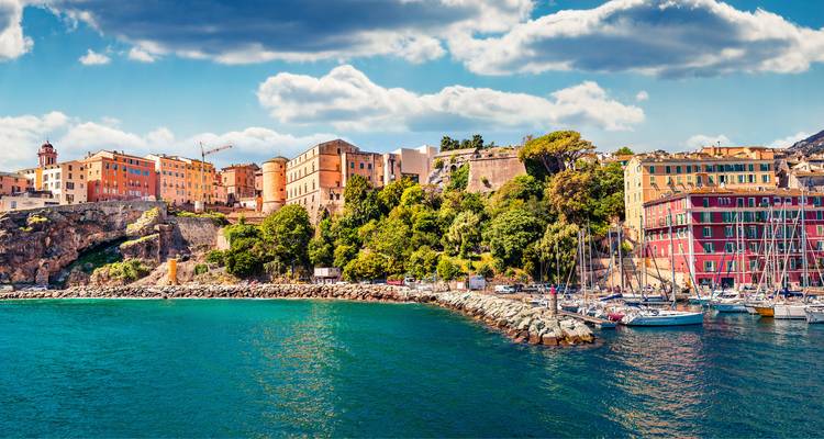 Port animé d'Alghero avec des bâtiments historiques colorés et des yachts sur une mer turquoise.