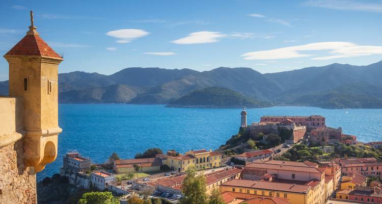 Vista elevada de los tejados de terracota de Portoferraio y el faro con el profundo mar Tirreno azul y las montañas al fondo