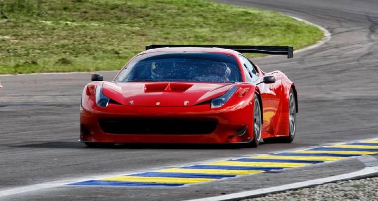 Een rode Ferrari raceauto scheurt met hoge snelheid over een bocht op het circuit op een zonnige dag.