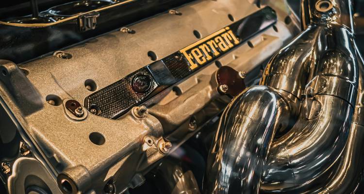Close-up van een gepoetste Ferrari-motor met metalen uitlaatonderdelen en logo.
