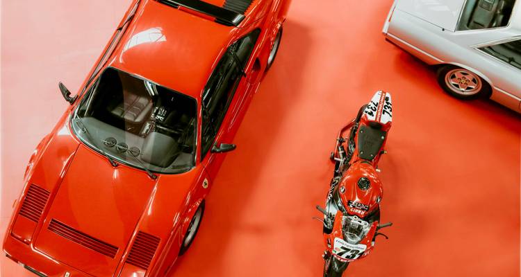 Bovenaanzicht van een klassieke rode Ferrari en racemotor op een felrode vloer.