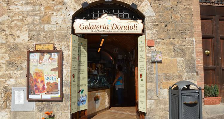 Stone facade of Gelateria Dondoli with open doorway and colorful signs in San Gimignano.