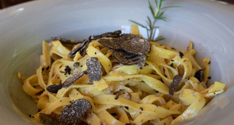 Tagliatelle pasta generously topped with shaved black truffles in a ceramic bowl.
