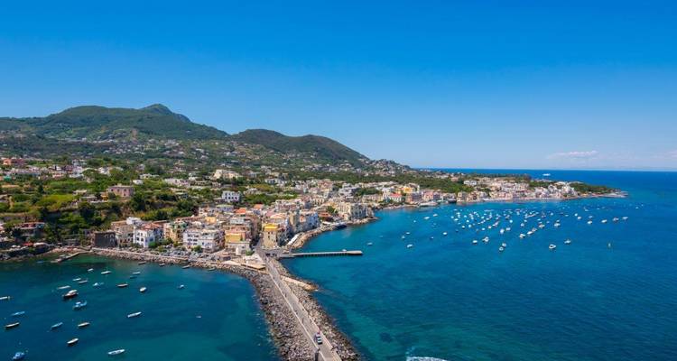 Luftaufnahme einer farbenfrohen Küstenstadt auf Ischia mit Booten, die die leuchtend blaue Tyrrhenische See prägen.