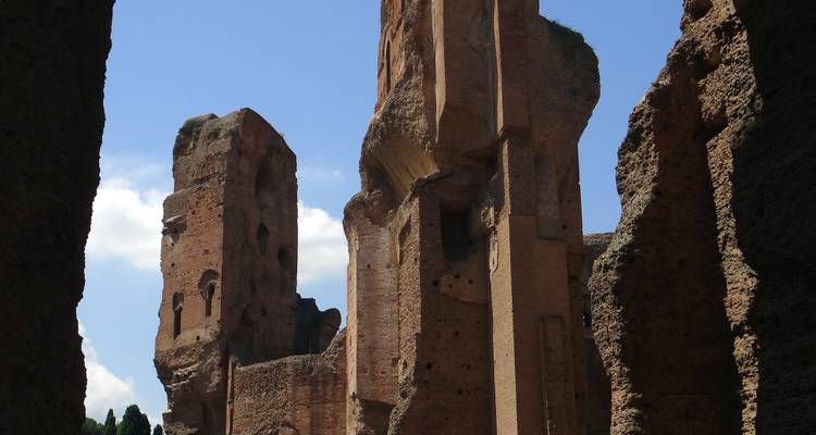 Towering ancient brick walls and arches of the Baths of Caracalla against blue sky.