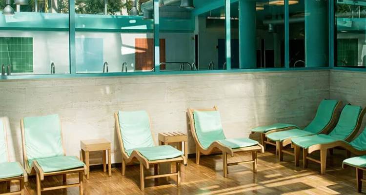 Simple indoor relaxation room with rows of empty mint-green lounge chairs by glass wall.