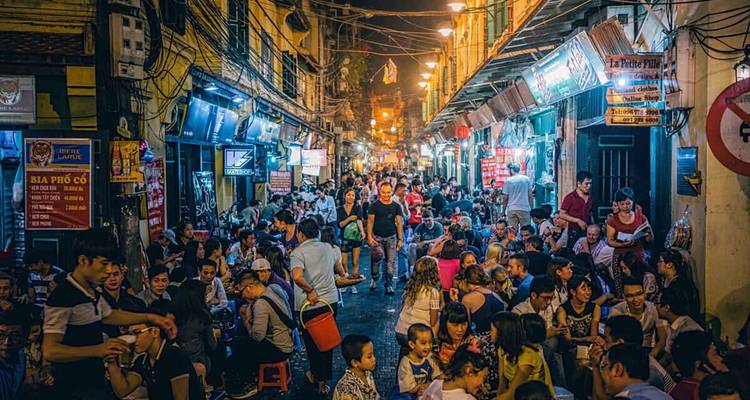 Drukke nachtlevensteeg in Hanoi's Oude Wijk vol met gasten en neonverlichting.