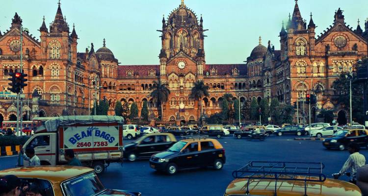 Druk verkeer voor het victoriaanse gotische Chhatrapati Shivaji Terminus bij schemering.